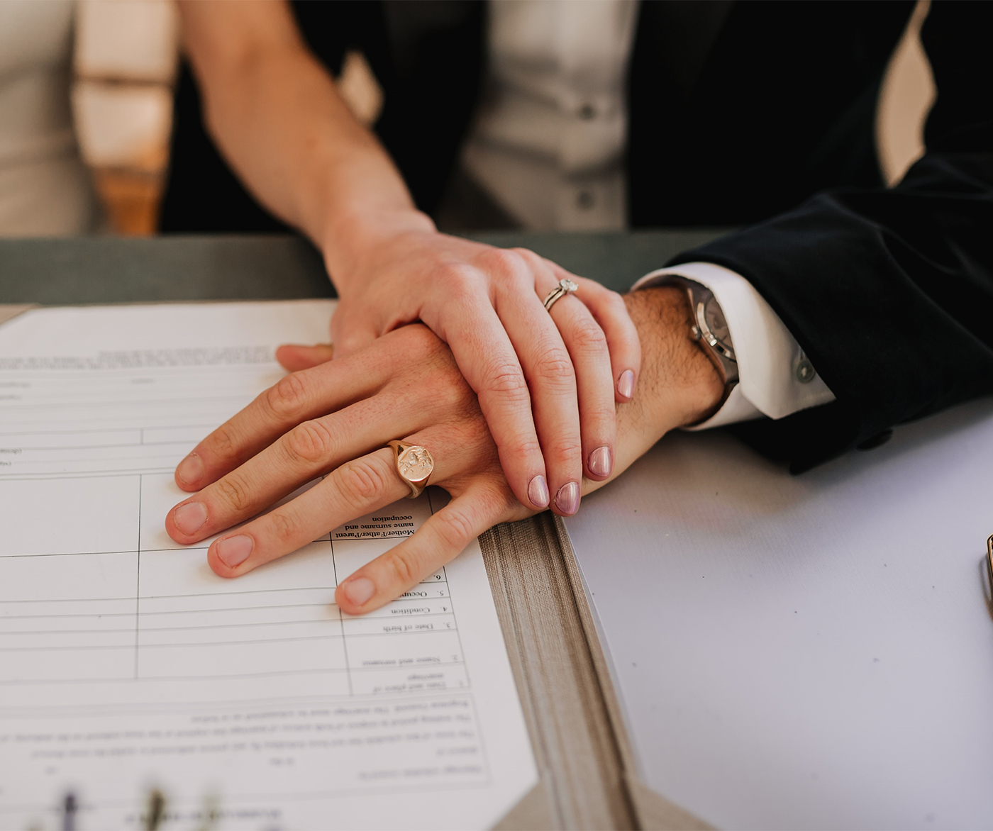 Newlywed couple with hands crossed on register with husband wearing engraved signet ring